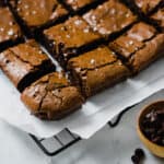 Fudgy brownies on cooling rack with small bowl of chocolate chips