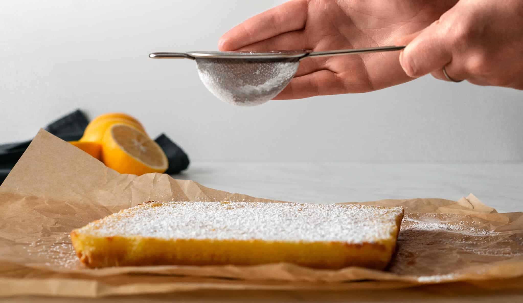 Meyer lemon bars being dusted with powdered sugar using a sifter