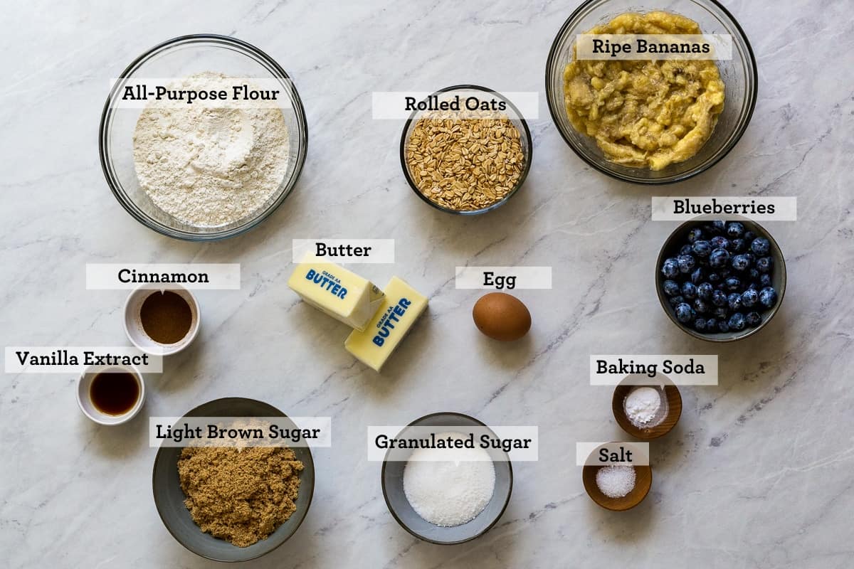 Overhead view of banana blueberry oat bar ingredients on a marbled background and labelled.