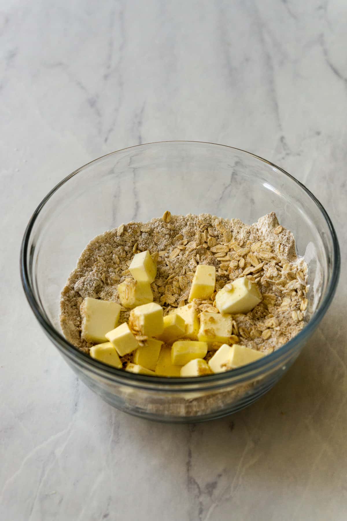Combined flour, rolled oats, cinnamon, brown sugar with the cubes of butter in a glass bowl.