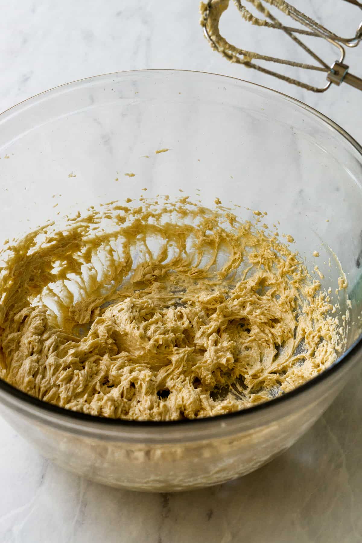 Wet ingredients for cookie base creamed together using a hand mixer in a glass bowl.