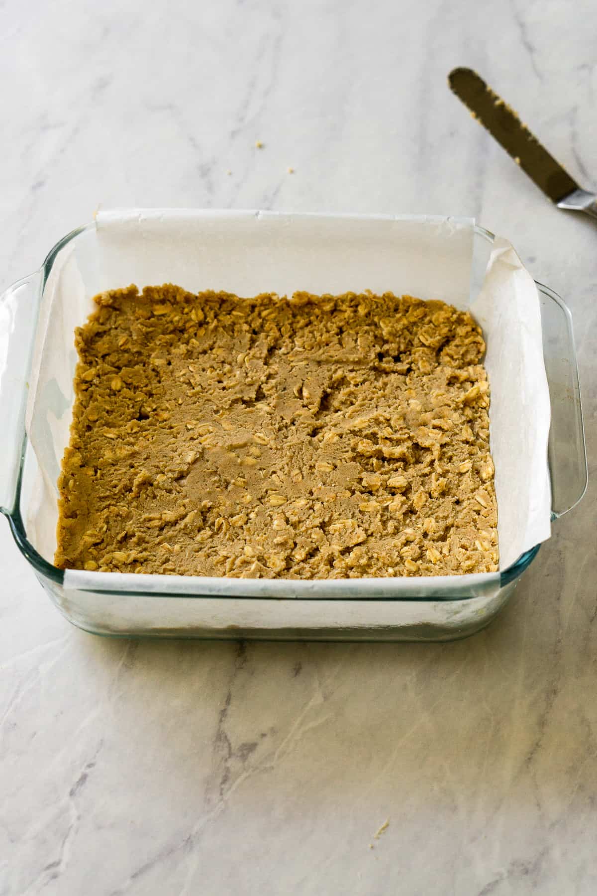 Cookie base dough pressed down in an 8x8 inch square glass pan lined with parchment paper.