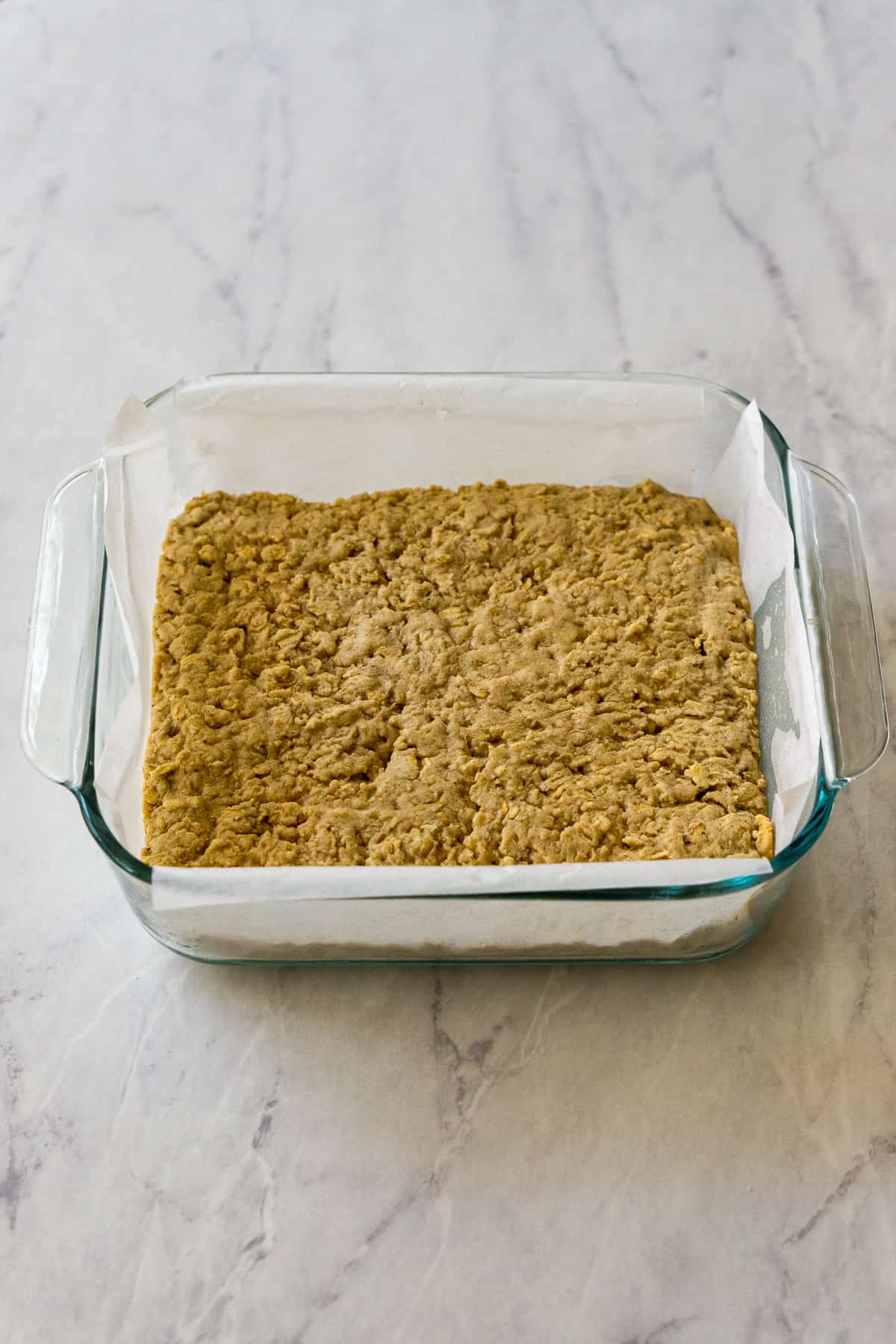 A baked cookie base in an 8x8 inch glass pan lined with parchment paper.