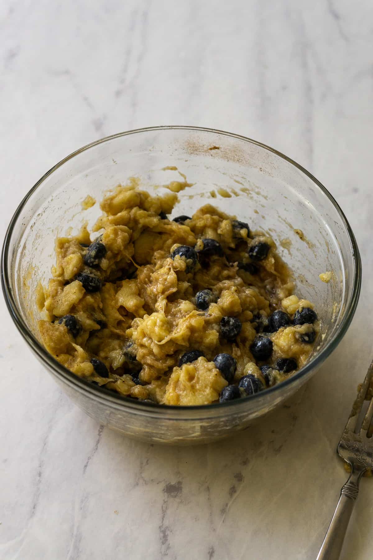 The mashed banana mixture combined with blueberries in a glass bowl. 